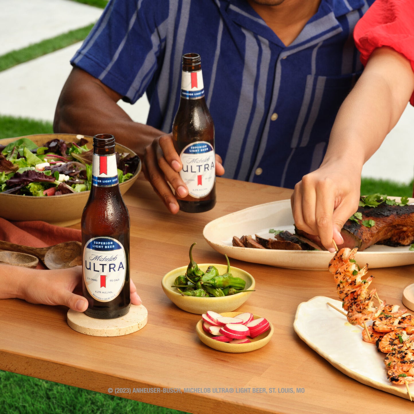 Two people sitting at a table with plates of food and bottles of Michelob Ultra beer.